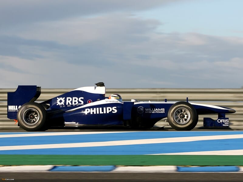 Voiture de Formule 1 Williams bleue et blanche roulant rapidement sur le circuit de Magny-Cours sous un ciel nuageux.