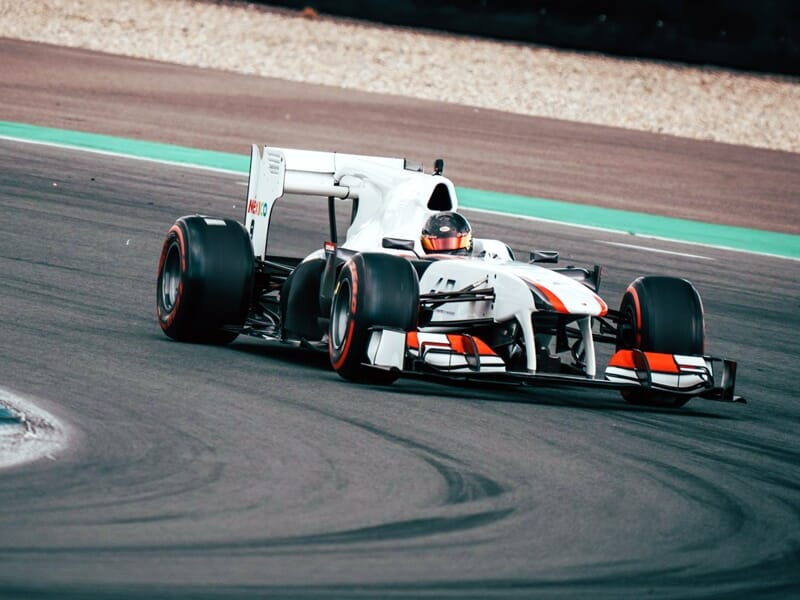 Voiture de course Formule 1 blanche avec détails orange prenant un virage serré sur le circuit de Magny-Cours.