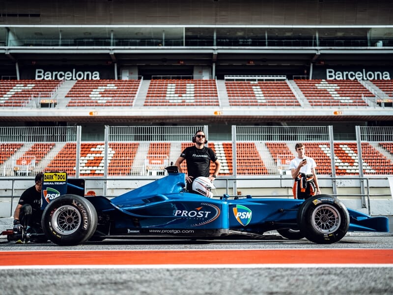 Voiture de Formule 1 bleue avec deux personnes debout sur la piste du circuit de Barcelone-Catalogne.