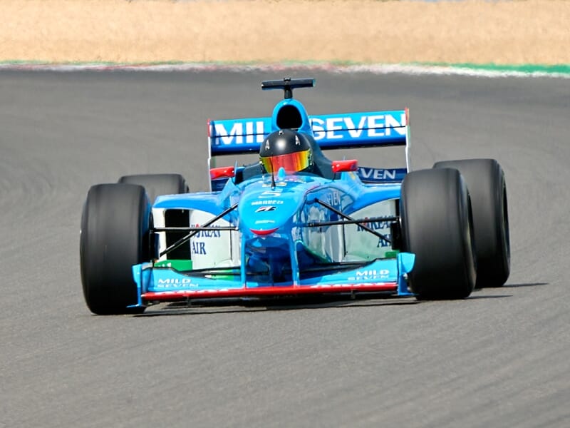 Voiture de Formule 1 bleue en pleine course sur le circuit, vue de face avec pilote casqué.