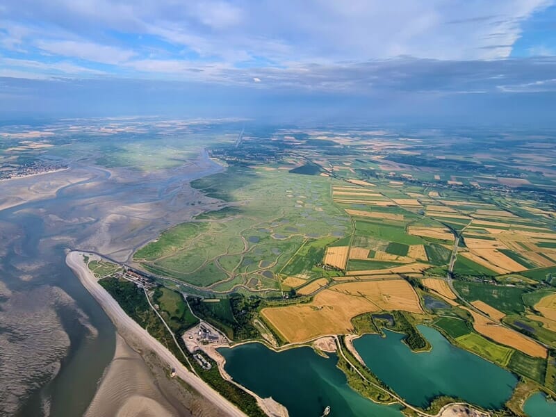 Vue aérienne d'un paysage côtier avec des champs agricoles, des plans d'eau lors d'un séjour insolite dans la Baie de Somme.