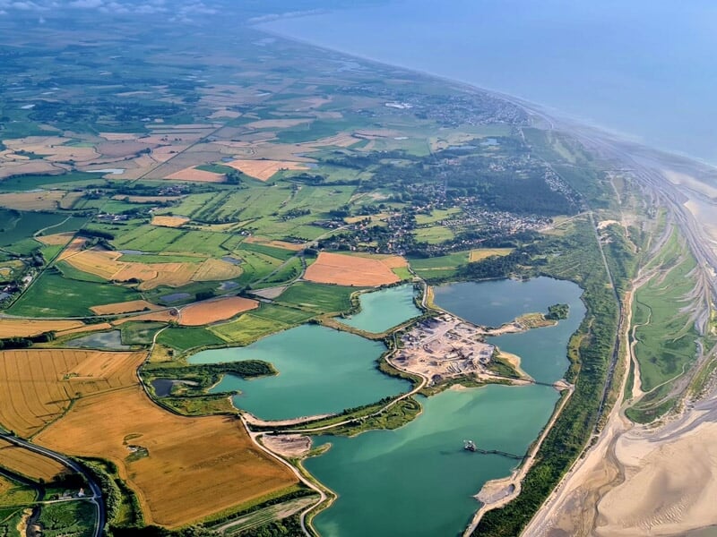 Vue aérienne d'un paysage côtier avec des plans d'eau, des champs cultivés et une plage sableuse lors d'un séjour insolite dans la Baie de Somme.