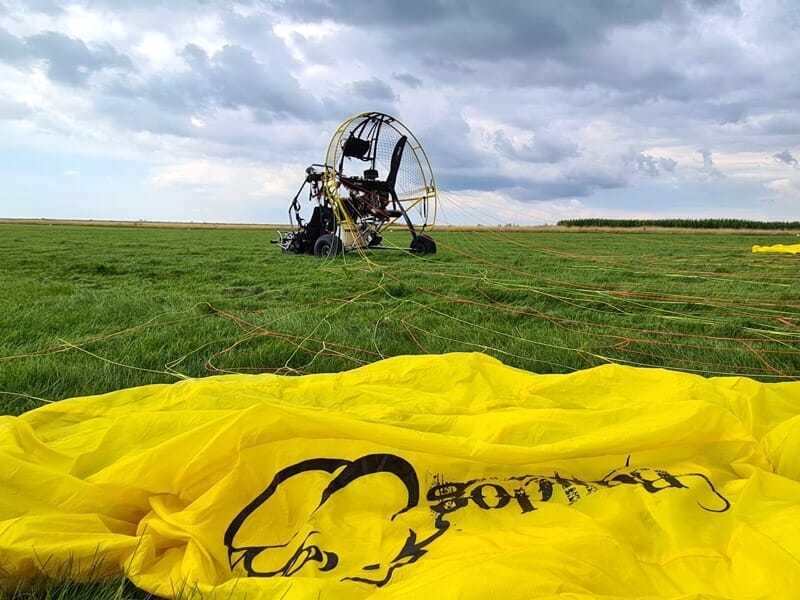 Paramoteur posé sur un champ vert avec une voile jaune étalée au premier plan lors d'un séjour insolite dans la Baie de Somme.