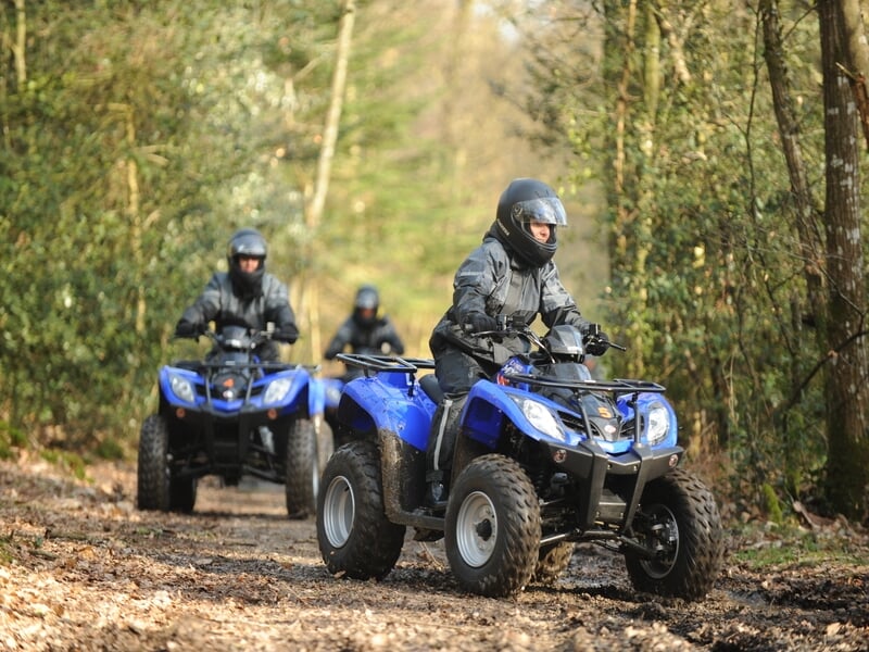 Trois personnes en quads bleus roulant sur un sentier forestier, équipés de casques et de vêtements de protection, profitant de l'exploration en nature.