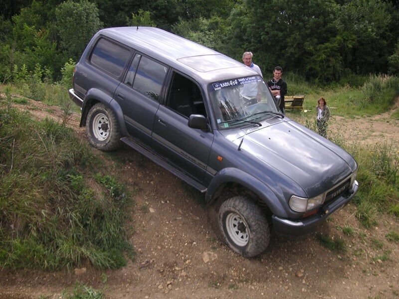 4x4 gris foncé descendant une pente raide dans un terrain boueux, trois personnes observant la manœuvre depuis le sommet de la colline.
