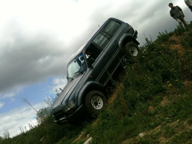 4x4 gris descendant une pente raide dans un paysage rural, avec un homme debout à côté observant la manœuvre.
