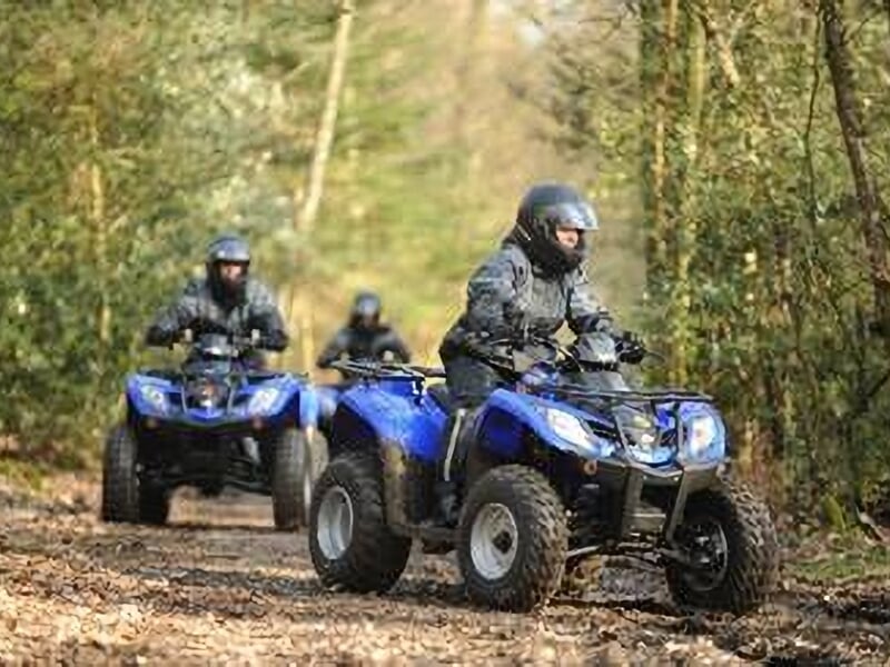 Trois personnes en quads bleus roulant sur un sentier forestier, équipés de casques et de vêtements de protection, explorant la nature.