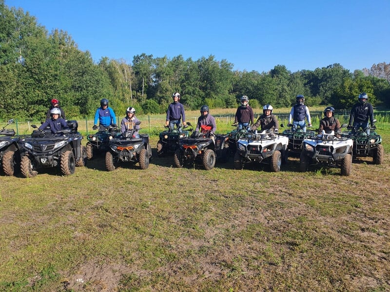 Groupe de personnes alignées sur des quads en plein air, portant des équipements de sécurité et des vêtements de sport. Les quads de différentes couleurs sont prêts pour une aventure en pleine nature 