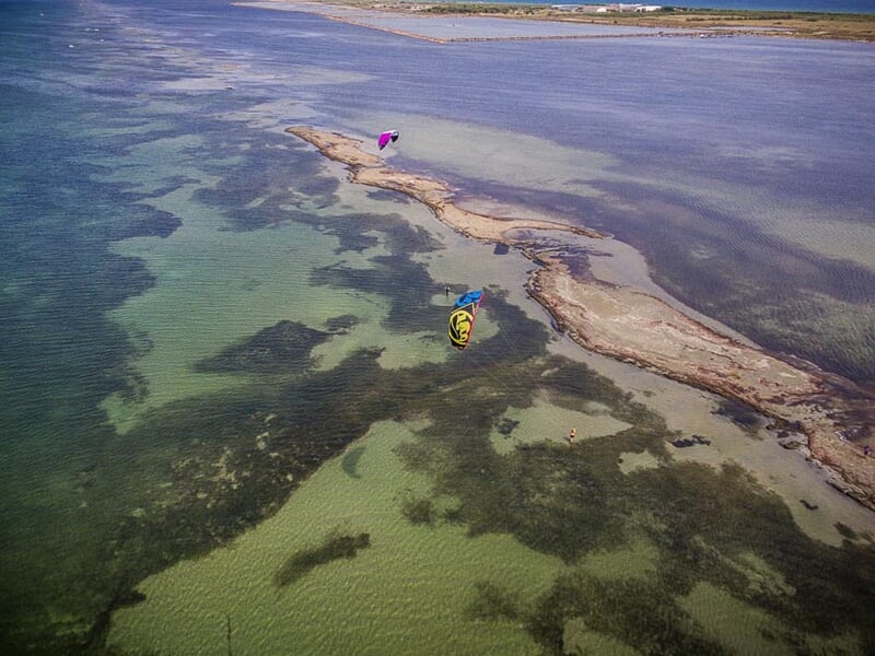 Vue aérienne du Bassin de Thau avec des kitesurfeurs colorés glissant sur l'eau claire et peu profonde.