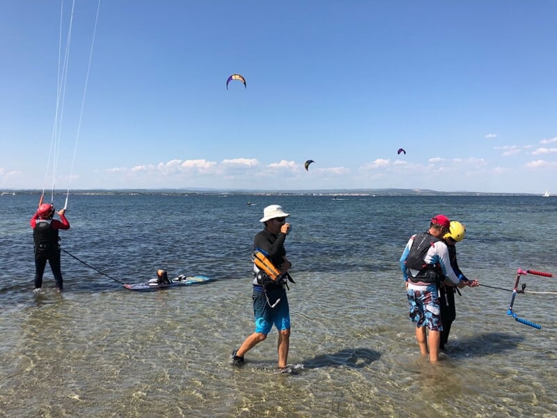 Groupe de kitesurfeurs en combinaison et casque s'entraîne dans l'eau peu profonde avec un instructeur.