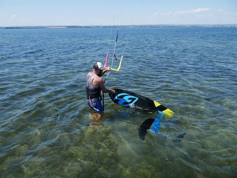 Une homme dans l'eau avec une planche de kitesurf, tenant une voile