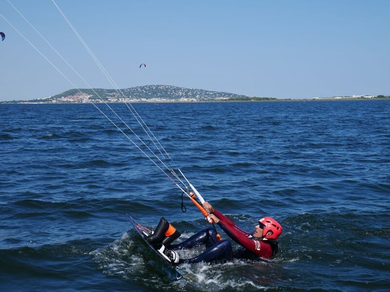 Une personne habillée de rouge, portant un casque, dans l'eau, en train de faire du kitesurf