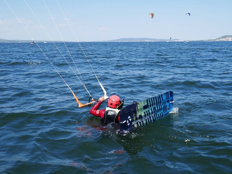 Un kitesurfer dans l'eau, avec un équipement rouge et une planche bleue