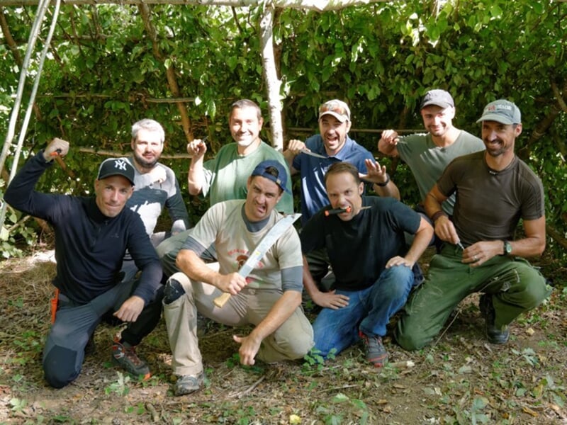 Huit hommes posant ensemble, souriants, dans un environnement naturel après un stage de survie.