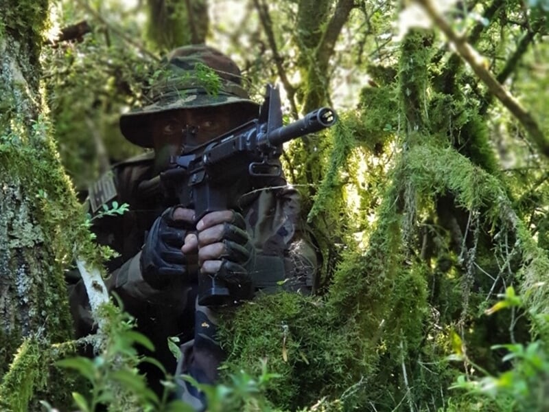 Soldat camouflé, armé, caché dans une végétation dense, prêt à tirer avec son fusil.