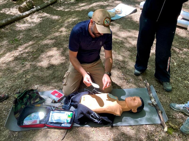 Formateur appliquant des électrodes de défibrillateur sur un mannequin de secourisme, matériel médical ouvert, en pleine forêt