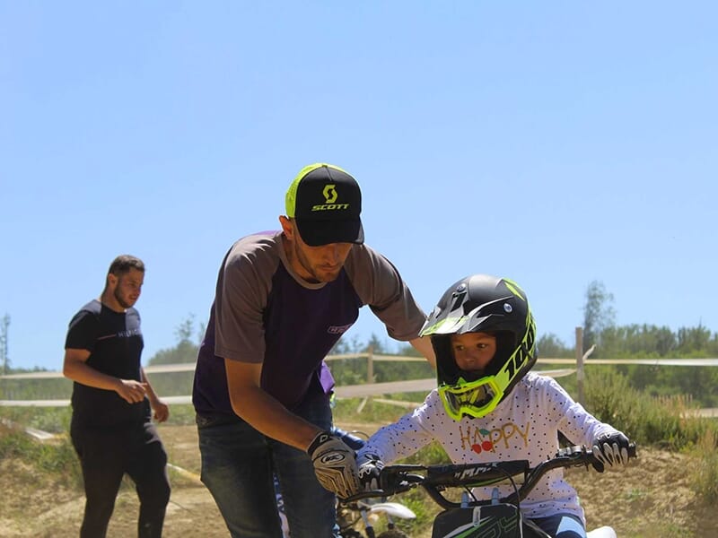 Un moniteur de motocross aide un enfant à piloter une moto de cross sur une piste école