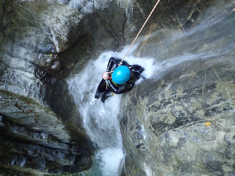 Personne en casque bleu descend en rappel dans un canyon rocheux avec un fort courant d'eau vive.