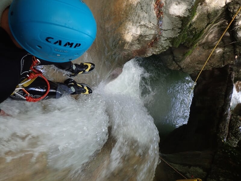 Vue plongeante d'une personne en casque bleu descendant une cascade d'eau vive en canyoning.