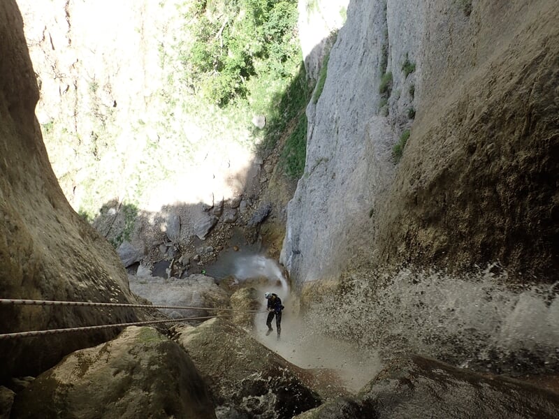 Personne descend en rappel dans un canyon étroit avec des parois rocheuses hautes et un fort débit d'eau.