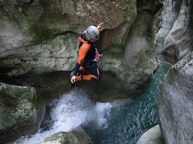 Personne en combinaison orange saute dans une eau profonde entourée de rochers dans un canyon étroit.