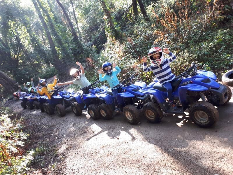 Groupe de personnes sur des quads bleus alignés sur un chemin en forêt, saluant la caméra joyeusement.