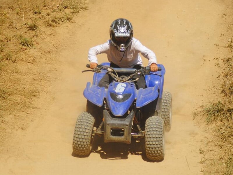 Enfant en casque conduisant un quad bleu sur un terrain sec et poussiéreux, vue de face.