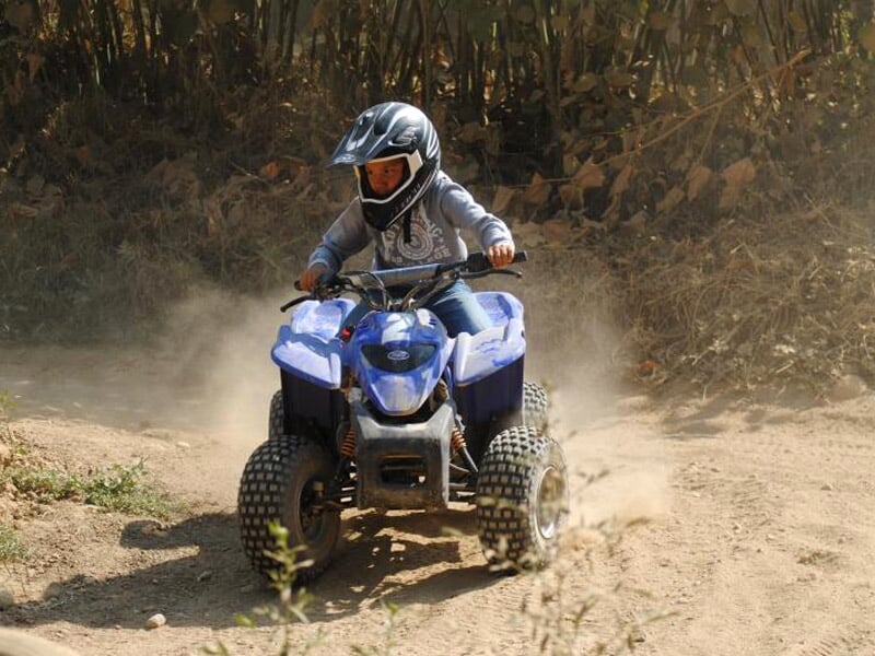 Personne en casque sur un quad bleu dérapant sur un chemin de terre entouré de végétation.