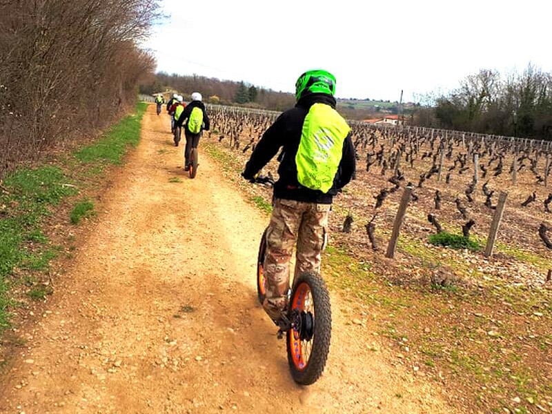 Personne en casque vert et veste jaune conduisant une trottinette électrique sur un chemin de terre.
