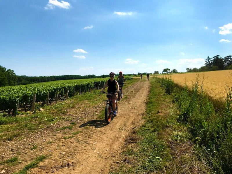 Groupe de personnes roulant à vélo sur un chemin de campagne entouré de champs et ciel bleu.