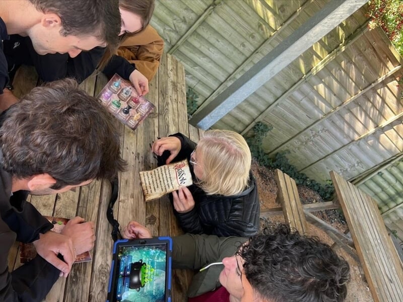 Groupe de personnes autour d'une table en bois examinant des objets et des documents pour résoudre une énigme.