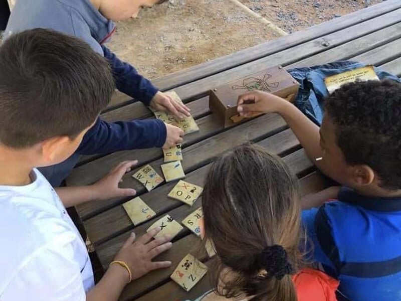 Enfants travaillant ensemble sur des morceaux de puzzle en bois disposés sur une table, avec une boîte au thème de pirates à proximité.