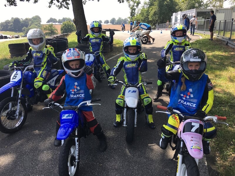 Groupe d'enfants en tenue de moto avec casques posent sur leurs motos sur un terrain de terre battue.
