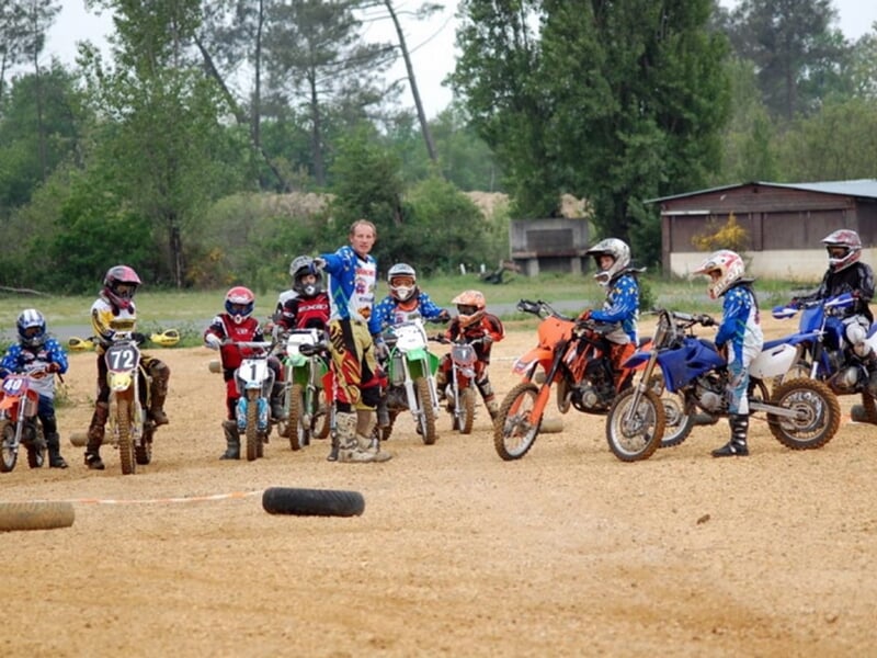 Groupe d'enfants en tenue de moto avec casques posent sur leurs motos sur un terrain de terre battue.