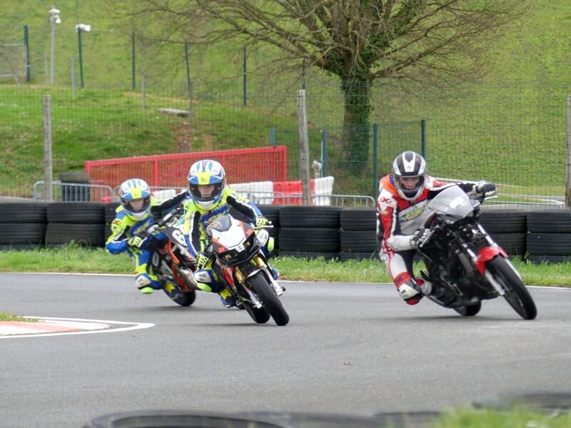 Groupe d'enfants en tenue de moto avec casques posent sur leurs motos sur un circuit asphalté en extérieur.