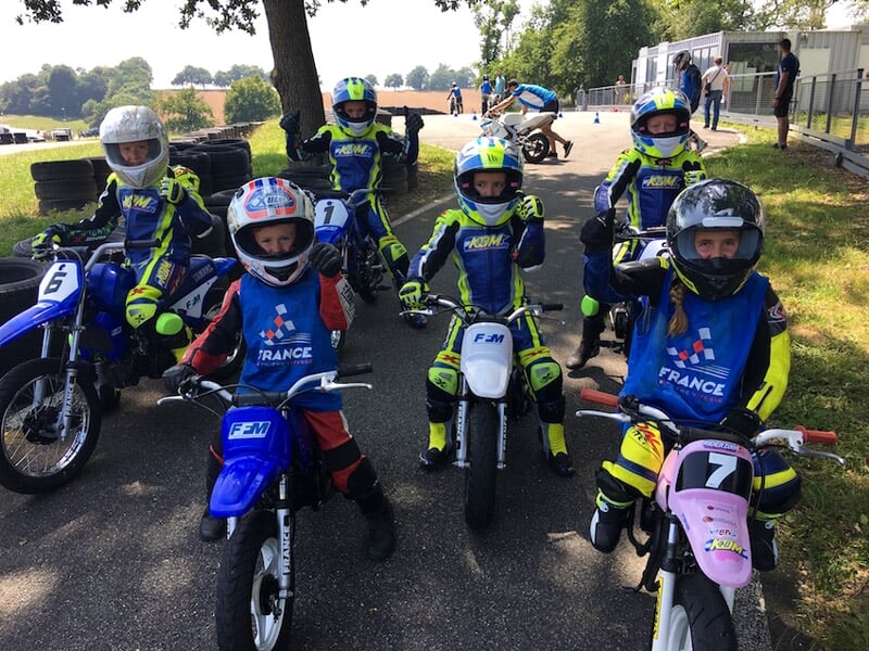 Trois motards en tenue de course prennent un virage serré sur un circuit de course asphalté.