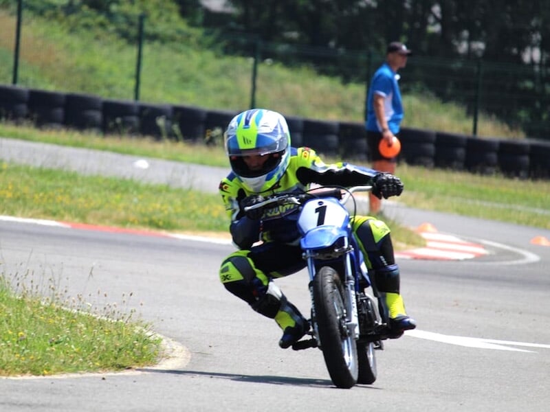 Groupe d'enfants en tenue de moto avec casques posent sur leurs motos sur un circuit asphalté en extérieur.