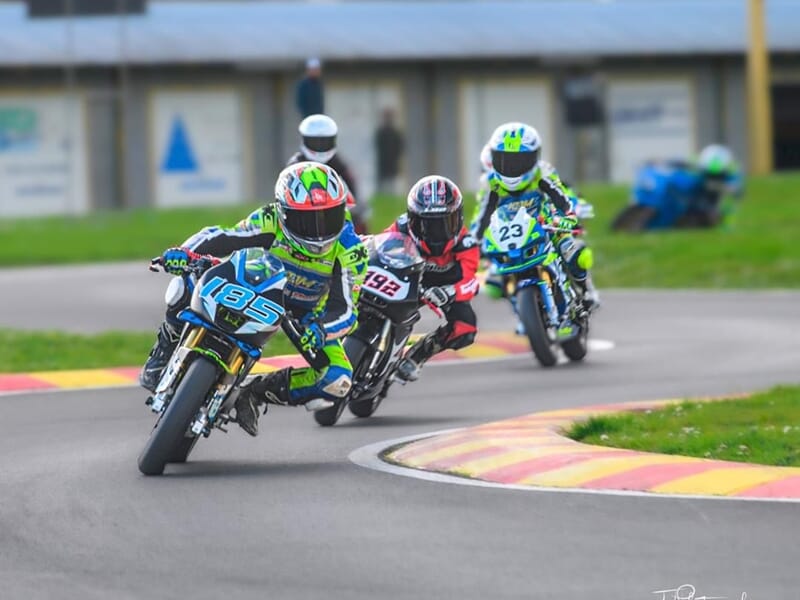 Quatre jeunes pilotes en combinaison de moto colorée prennent un virage serré lors d'un stage moto enfant.