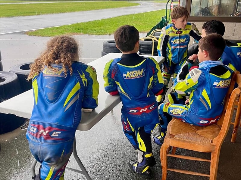 Groupe d'enfants en combinaison de moto bleue et jaune discutent lors d'un stage moto enfant.