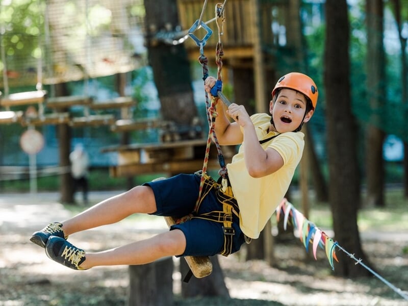 Jeune garçon avec casque et harnais glissant sur une tyrolienne dans un parc d'accrobranche en plein air.