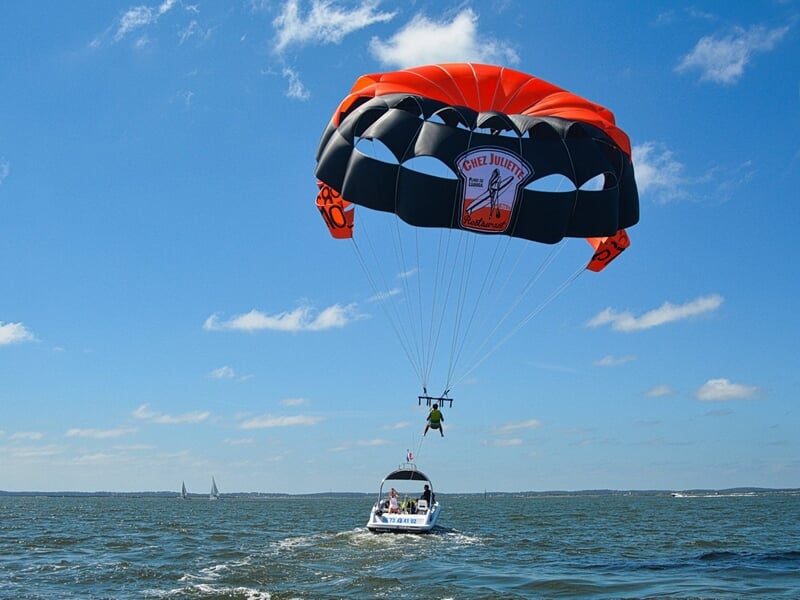 Personne en parachute ascensionnel tirée par un bateau blanc sur une mer calme sous un ciel bleu avec quelques nuages.