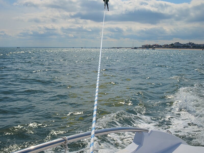 Corde de traction vue depuis un bateau sur une mer agitée, avec une personne en parachute ascensionnel en hauteur.