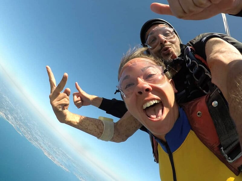 Saut en parachute en tandem avec expressions de joie, selfie en plein ciel, vue dégagée sur l'horizon et la mer