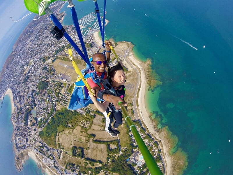 Saut en parachute tandem, vue aérienne de la côte, femme et instructeur en parachute ouvert, tenant une perche à selfie.