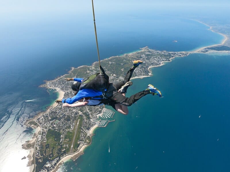 Saut en parachute tandem, homme et instructeur en chute libre au-dessus d'une côte, vue aérienne détaillée du littoral et de la mer.