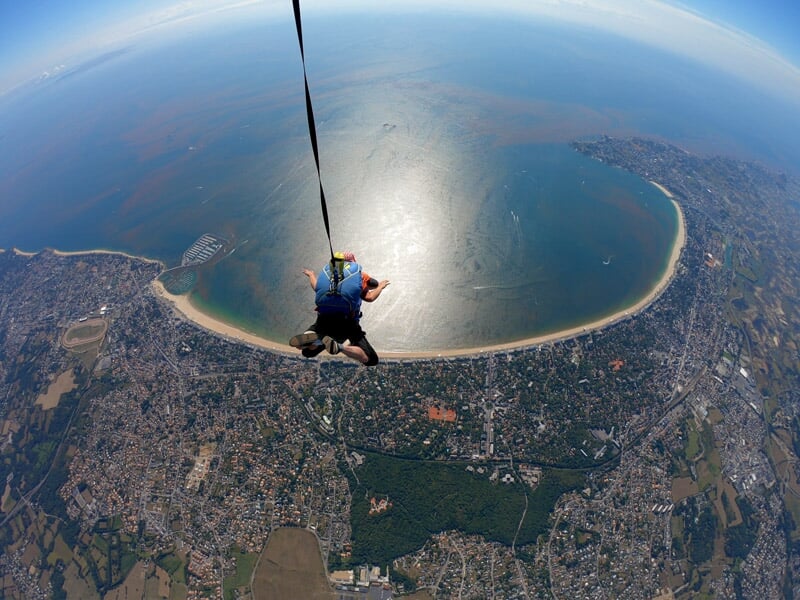 Parachutiste seul descendant vers une baie lumineuse, vaste panorama d'une plage, d'une ville et d'une campagne verdoyante