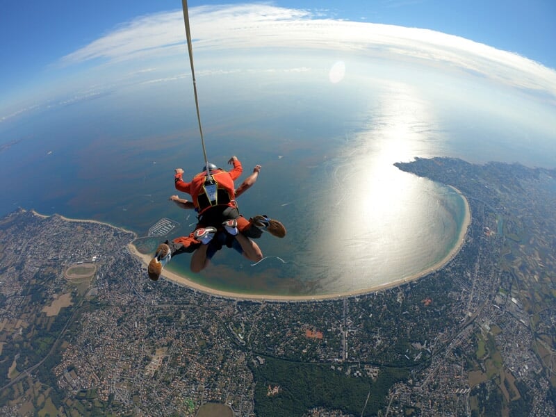 Vue aérienne spectaculaire d'un saut en parachute en tandem, reflet du soleil sur l'eau, paysage urbain et rural entourant la baie