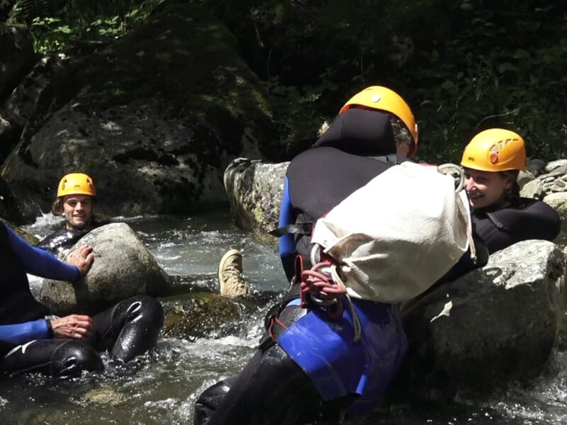 Groupe de personnes en tenue de canyoning assises et discutant dans une rivière rocheuse en forêt.