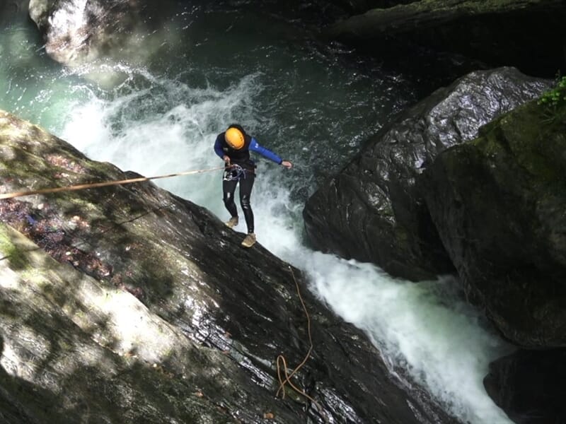 Personne en combinaison de canyoning descend en rappel le long d'une cascade puissante dans un canyon.