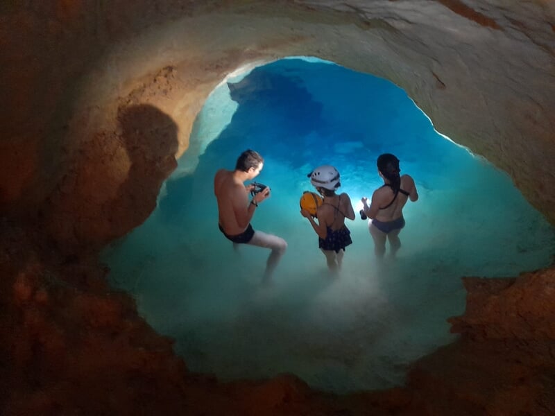 Trois personnes dans une grotte sous-marine, éclairées par une lumière bleue, explorant l'eau claire.